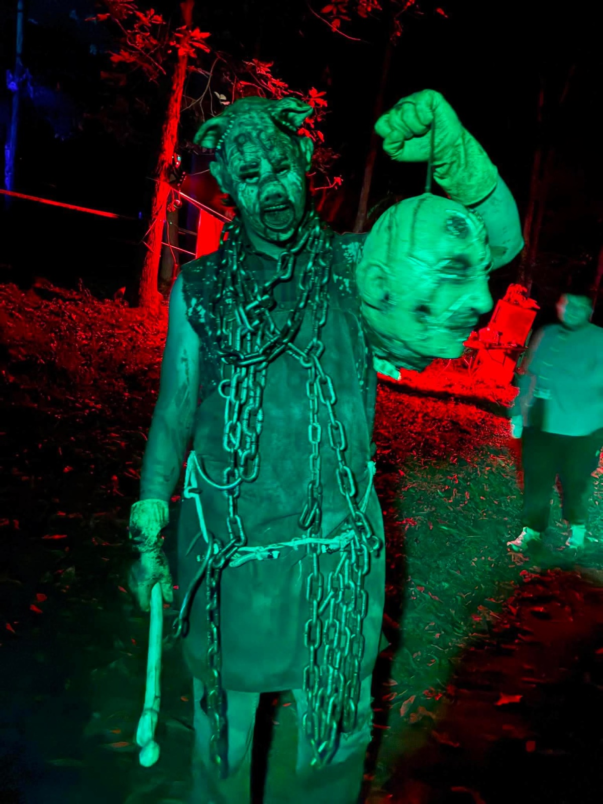 The pig-masked butcher holding a severed head under green light
