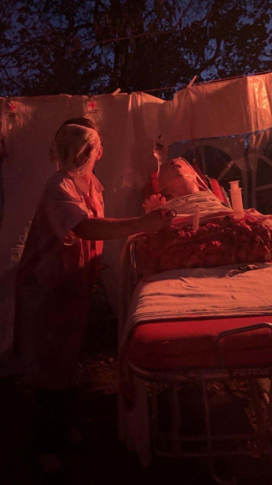 A nurse tends to a patient on a gurney in the outdoor asylum ward scene